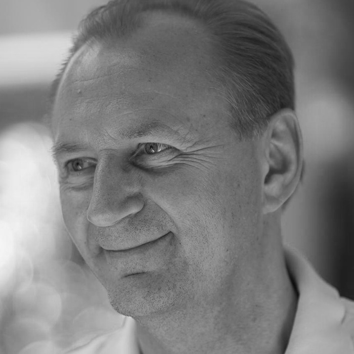 Black and white close-up portrait of a middle-aged man with short hair looking slightly to the side and smiling softly.